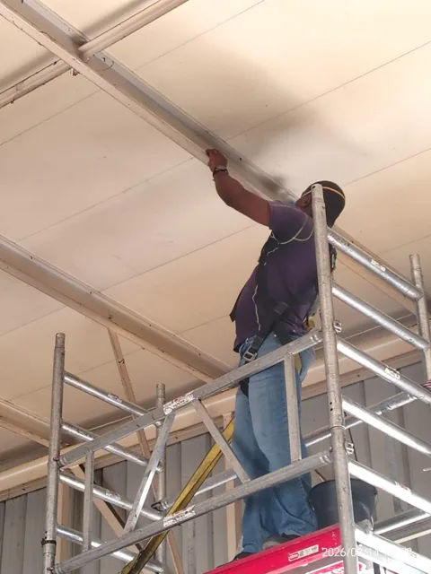 Worker on a scaffold attending to a ceiling panel and support rail
