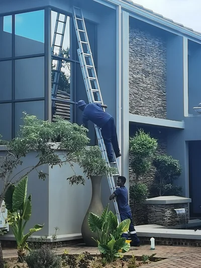 Window cleaners on a ladder cleaning tall exterior windows of a home