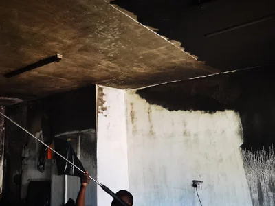 Operator pressure cleaning soot from a fire damaged ceiling and wall